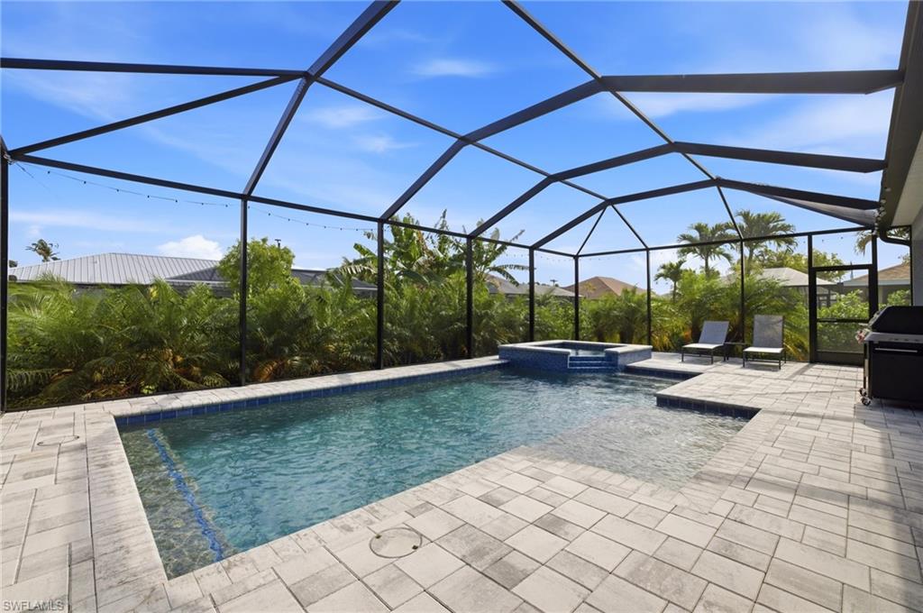 Screened patio featuring a swimming pool with integrated spa, paver decking, and mature tropical landscaping