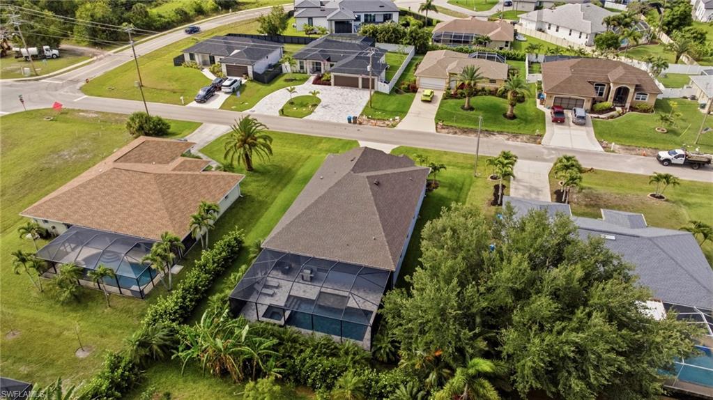 Aerial perspective showcasing a single-story residence with a screened-in pool enclosure, surrounded by mature landscaping and a green lawn