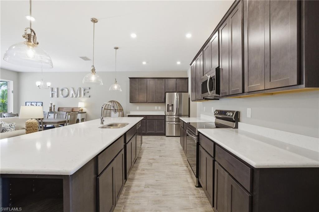 Modern kitchen featuring an expansive center island with an undermount sink, white countertops, dark wood cabinetry, and stainless steel appliances