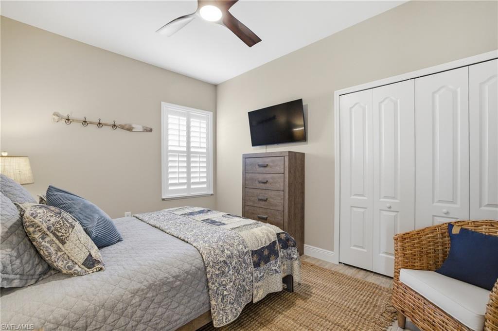 Bedroom featuring plantation shutters, wood-finish flooring, a ceiling fan with integrated lighting, and bi-fold closet doors