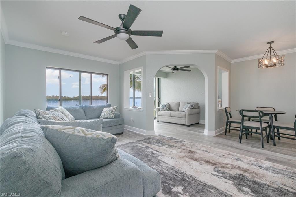 Living room featuring baseboards, ornamental molding, wood finished floors, arched walkways, and ceiling fan with notable chandelier