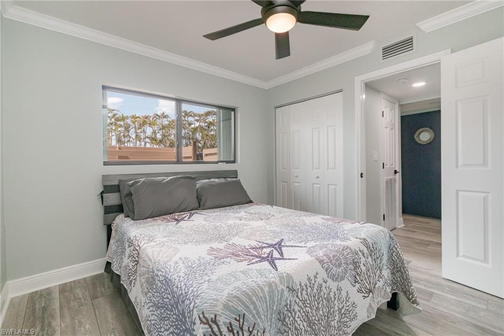 Bedroom featuring a closet, visible vents, light wood-style flooring, baseboards, and ornamental molding