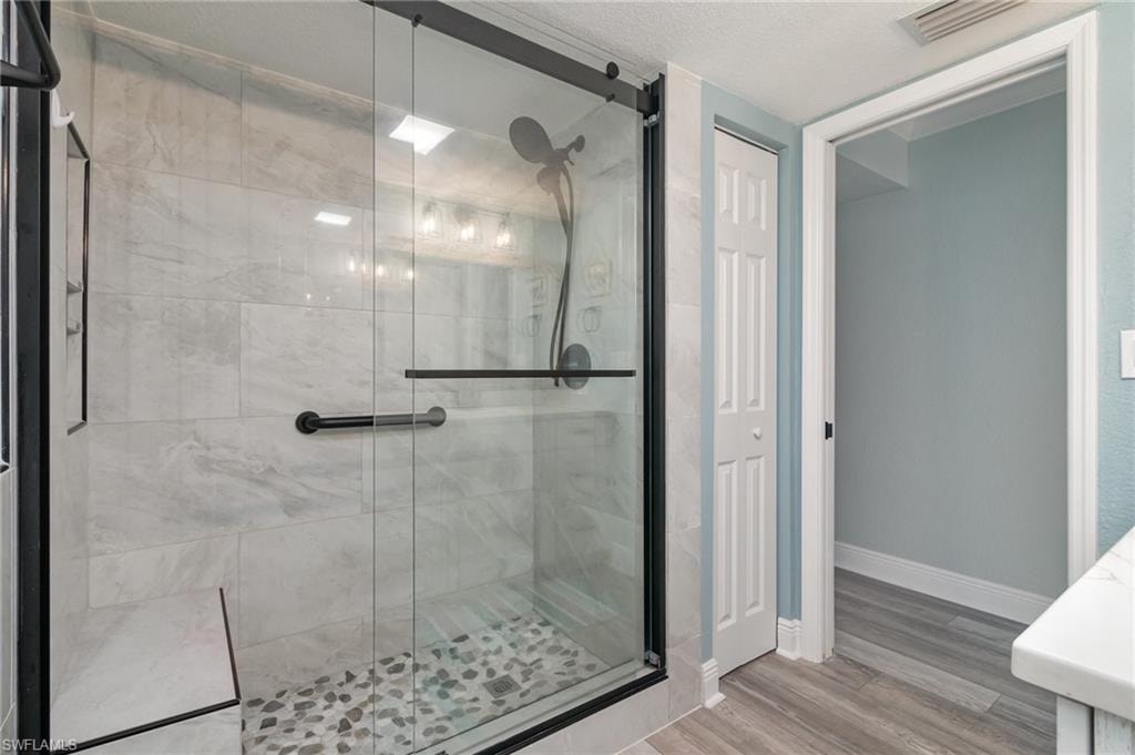 Bathroom featuring a shower stall, baseboards, visible vents, and wood finished floors