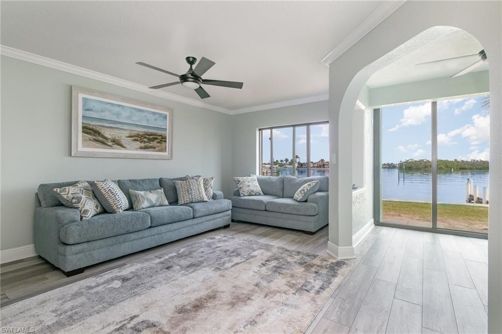 Living room with arched walkways, ceiling fan, ornamental molding, and a healthy amount of sunlight