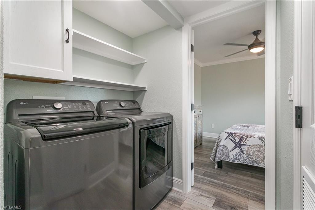 Laundry room with a ceiling fan, wood finished floors, washing machine and clothes dryer, baseboards, and cabinet space