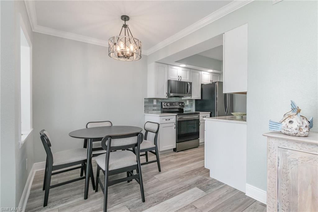 Kitchen featuring crown molding, light wood-type flooring, a chandelier, backsplash, and appliances with stainless steel finishes