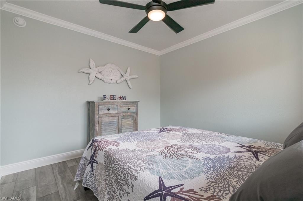 Bedroom featuring baseboards, crown molding, wood finished floors, and a ceiling fan