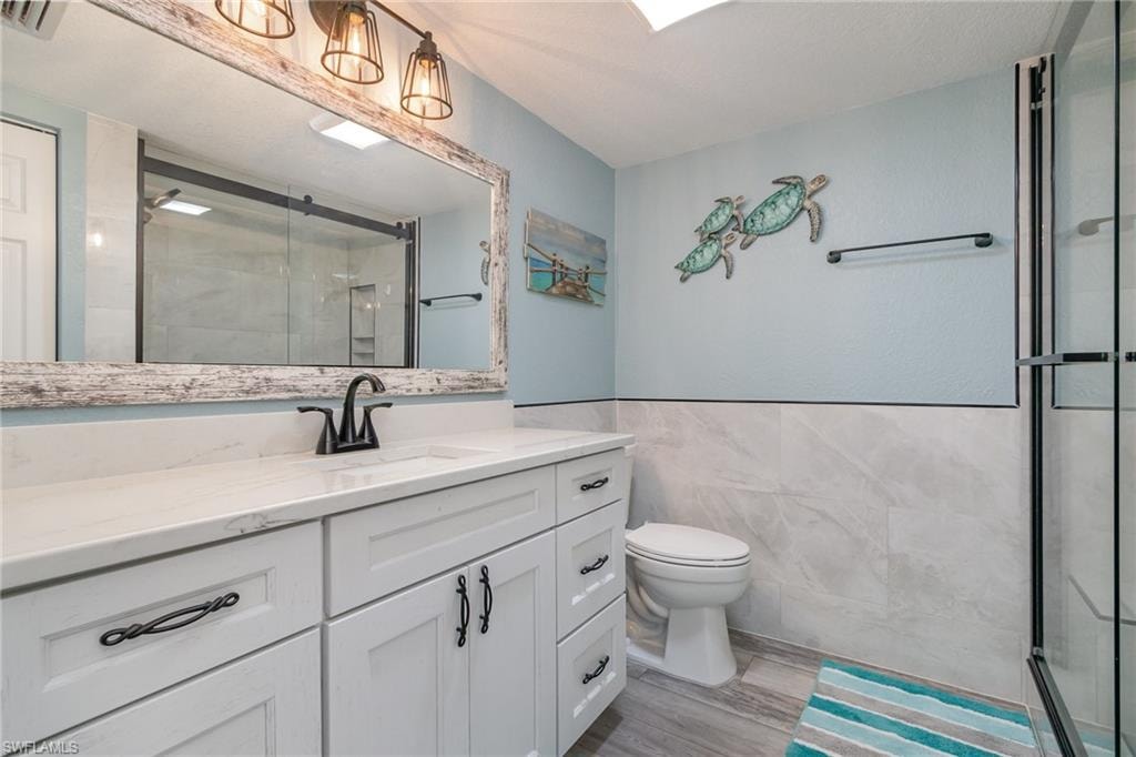 Full bathroom with a stall shower, toilet, vanity, and tile walls