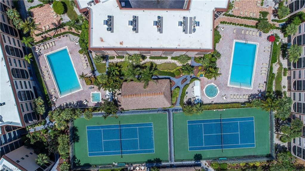 Expansive outdoor recreational area featuring two tennis courts, two swimming pools, and a spa, surrounded by lush landscaping and mature palm trees