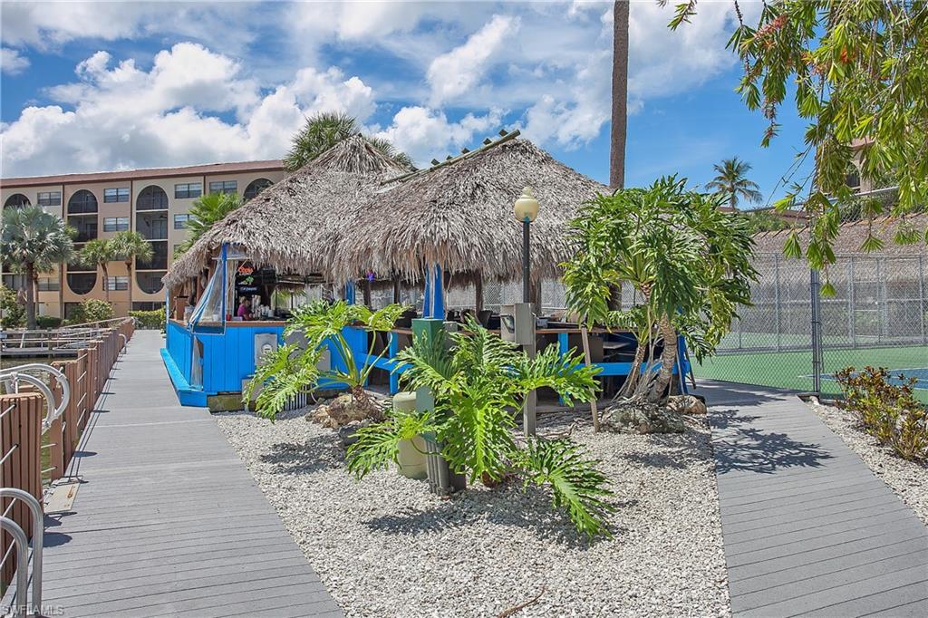 Thatched-roof bar structure with blue accents, surrounded by decorative landscaping and gravel