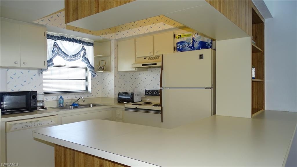 Kitchen featuring a peninsula countertop, white appliances, and ample cabinetry