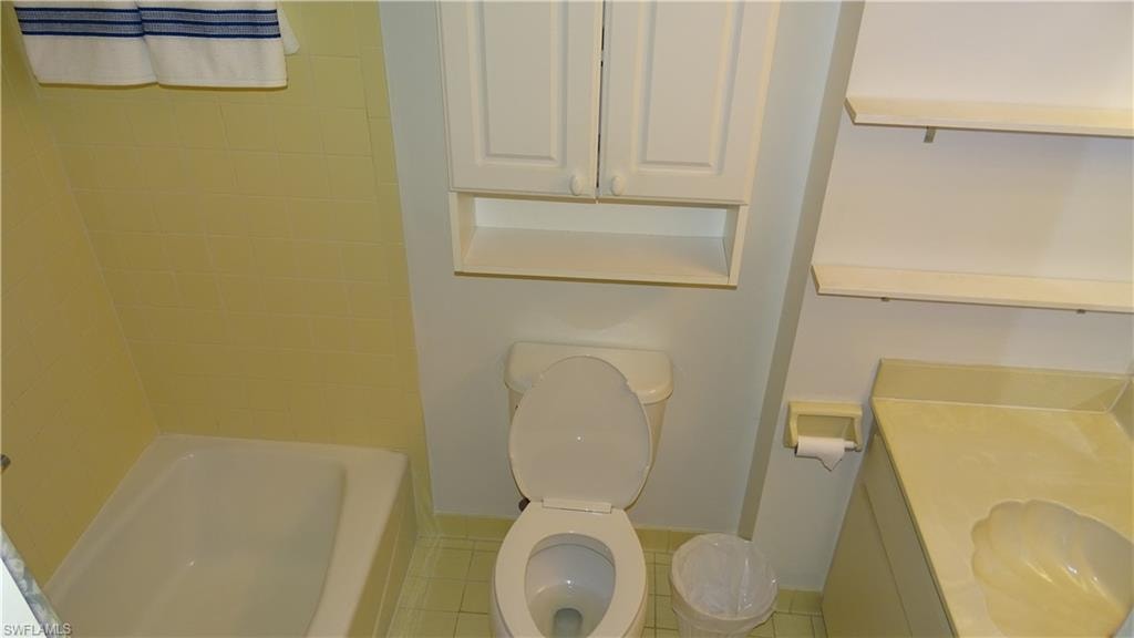 Bathroom featuring a white bathtub with yellow tiled surround, toilet, and a vanity with an integrated sink