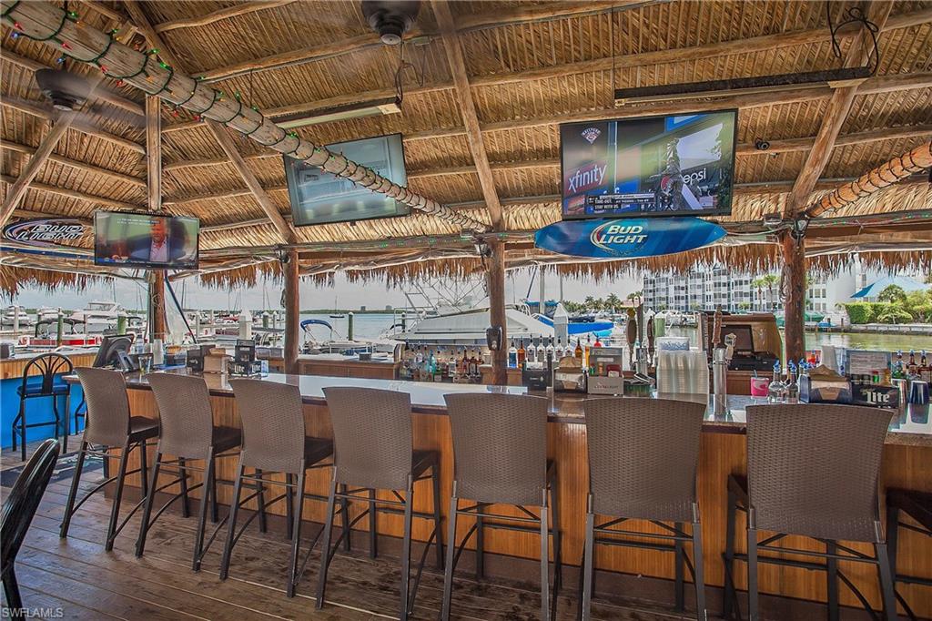 Tiki-style bar featuring a thatched roof, wood-finish flooring, and multiple mounted televisions