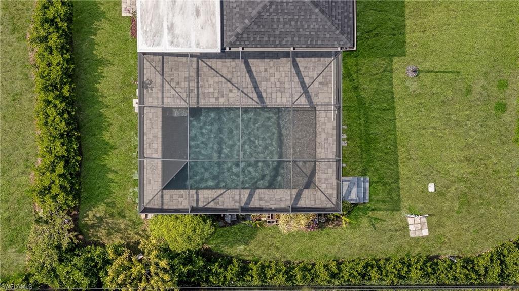 Screened swimming pool enclosure with paver decking, surrounded by a manicured lawn and mature privacy hedges