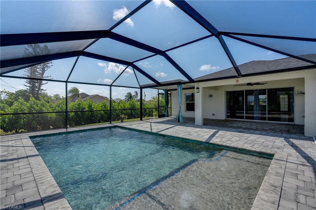 Screened-in pool area featuring a rectangular pool with an integrated spa, paver deck, and a covered lanai