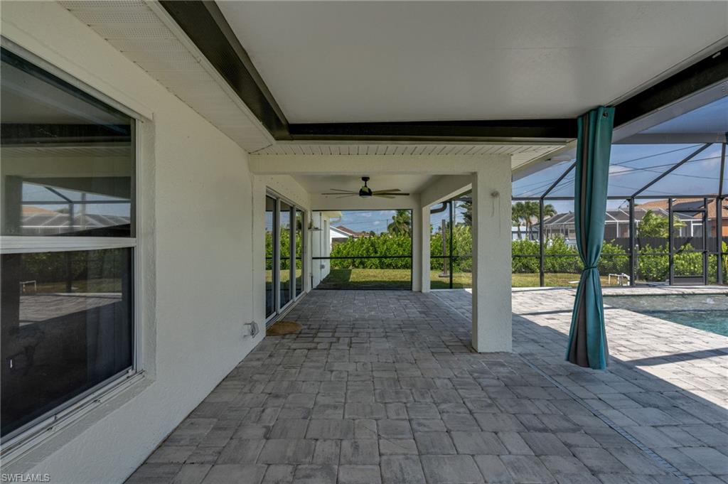 Spacious screened lanai featuring extensive paver flooring, overhead ceiling fan, and direct access to the pool area