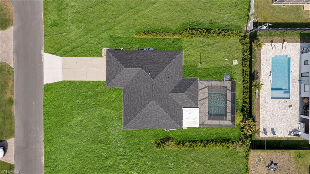 Single-story residence featuring a dark shingle roof, a screened-in pool enclosure, and an expansive concrete driveway