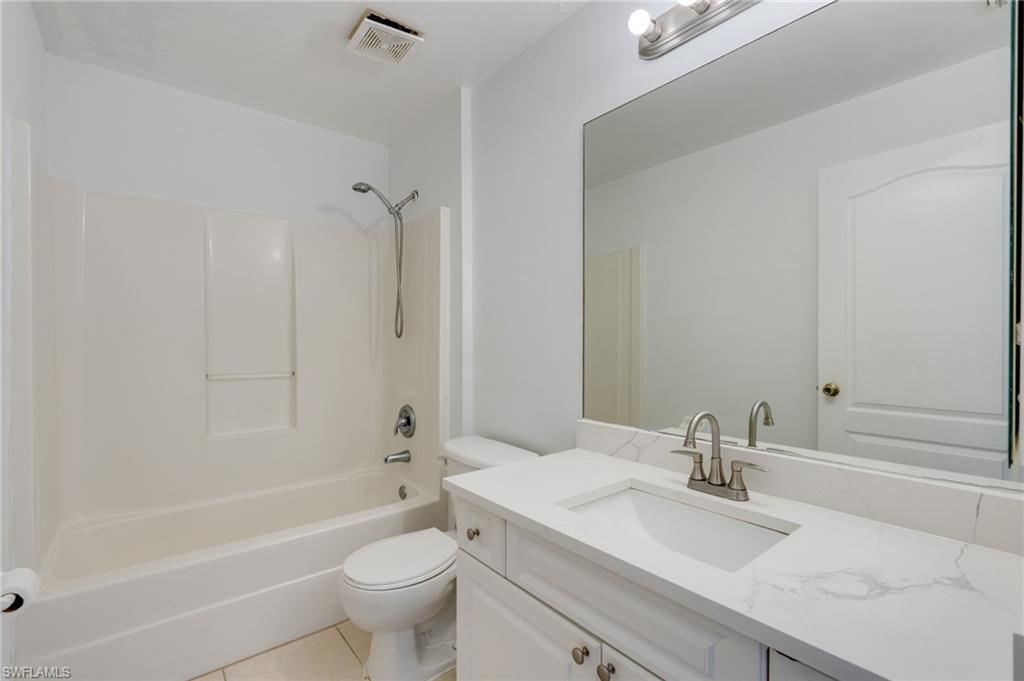 Bathroom featuring a white bathtub/shower combination, a vanity with a white countertop and integrated sink, a large wall-mounted mirror, and tile flooring