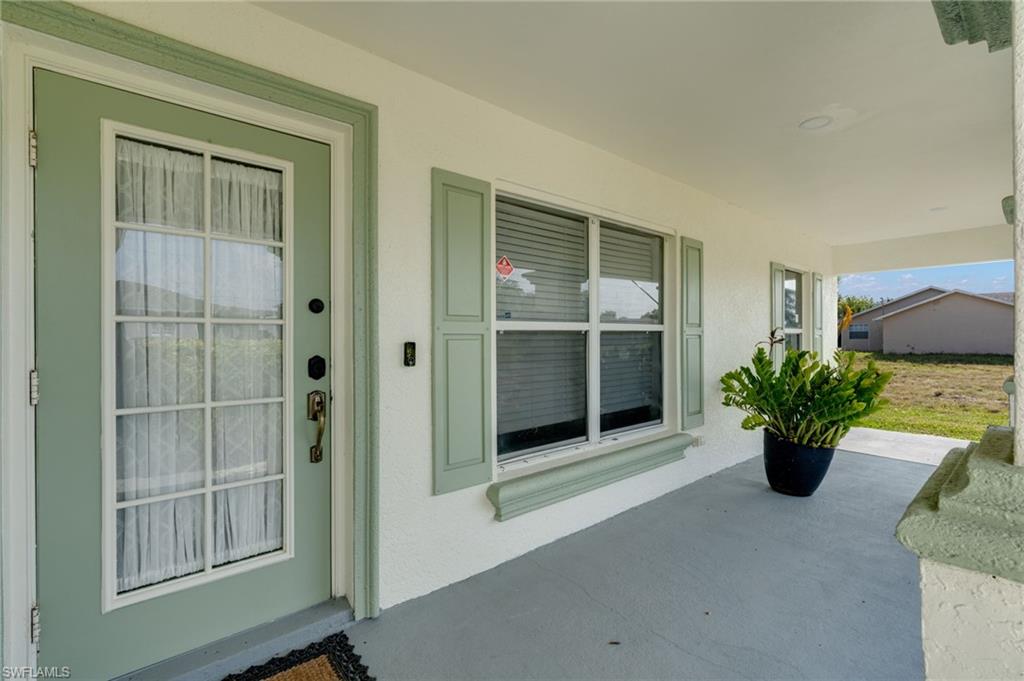 Covered entry featuring a transom window above the front door, glass-paneled front door, window shutters, and stucco exterior finish