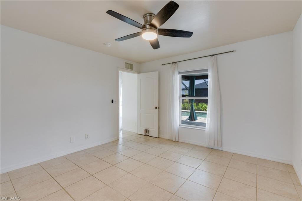 Room featuring neutral tile flooring, white walls, a ceiling fan with integrated lighting, and a window overlooking a screened pool area
