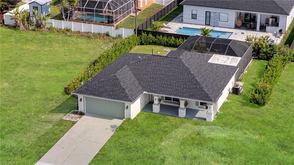 Single-story residence featuring a dark shingle roof, attached garage with a light green door, concrete driveway, and a screened-in rear patio
