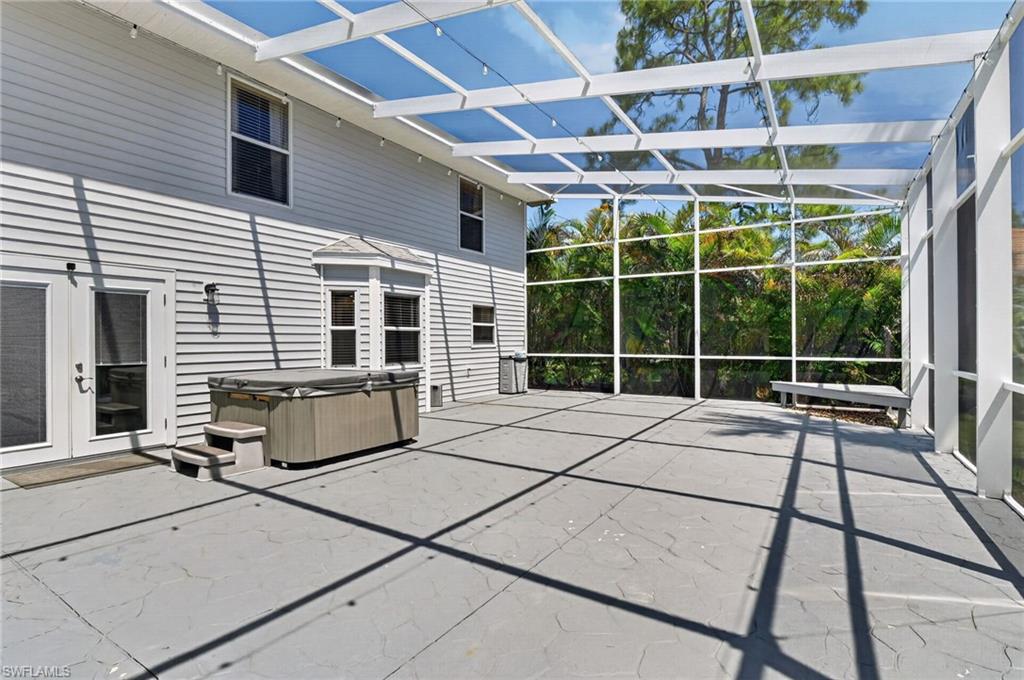 Expansive screened enclosure featuring a concrete patio, hot tub, and multiple entry points to the residence