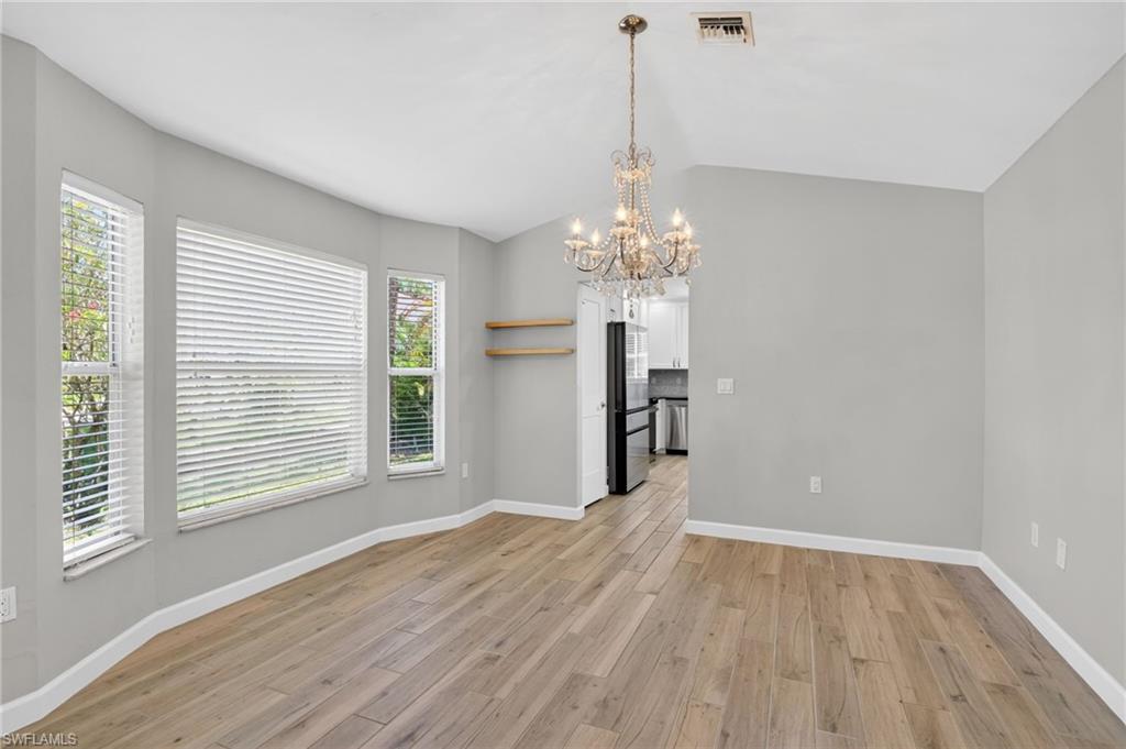 Spacious room featuring wood-finish flooring, a tiered crystal chandelier, and a bay window configuration with horizontal blinds