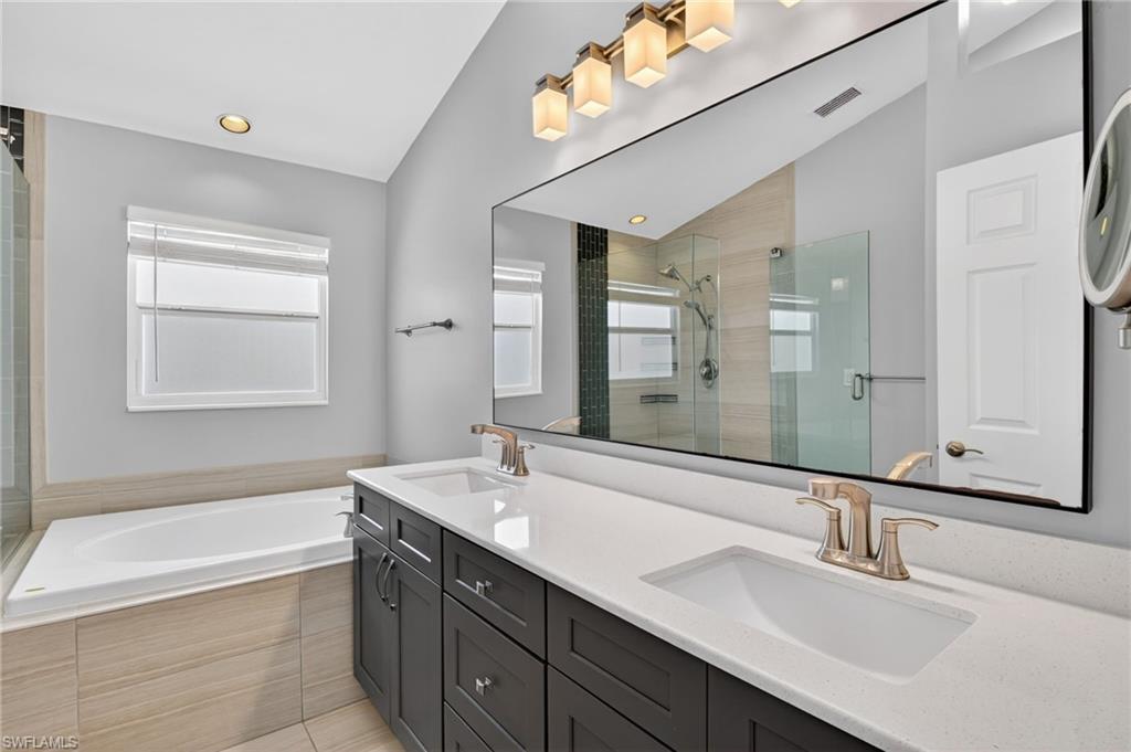 Bathroom featuring a spacious double vanity with white countertops and dark wood cabinetry, a large soaking tub with tiled surround, and a glass-enclosed shower with tiled walls