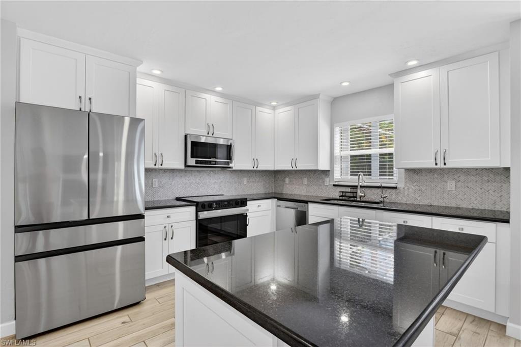 Modern kitchen featuring white shaker cabinetry, dark countertops, stainless steel appliances, a tile backsplash, and a central island