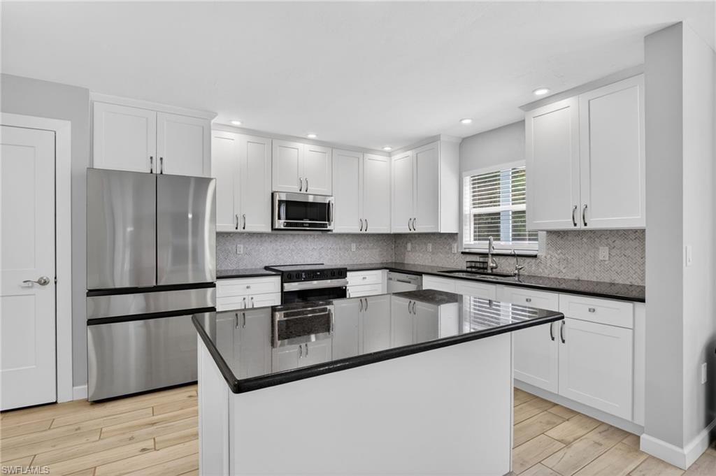 Contemporary kitchen featuring a central island, white shaker cabinetry, stainless steel appliances, dark countertops, and a mosaic tile backsplash