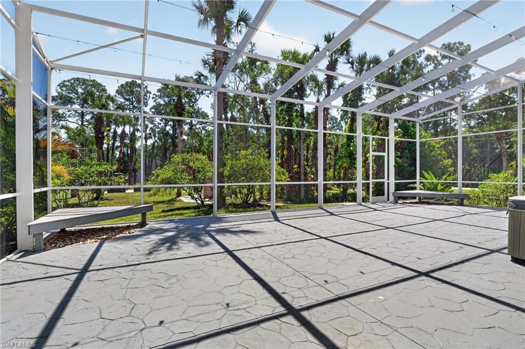 Expansive screened enclosure featuring a textured concrete patio, two built-in benches, a separate door, and overhead string lighting