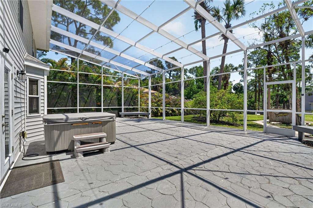 Expansive screened enclosure featuring a hot tub, textured patio flooring, and direct access to the interior via a glass-paneled door