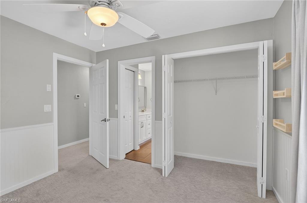 Carpeted room featuring wainscoting, a ceiling fan with integrated lighting, and a bi-fold closet with wire shelving