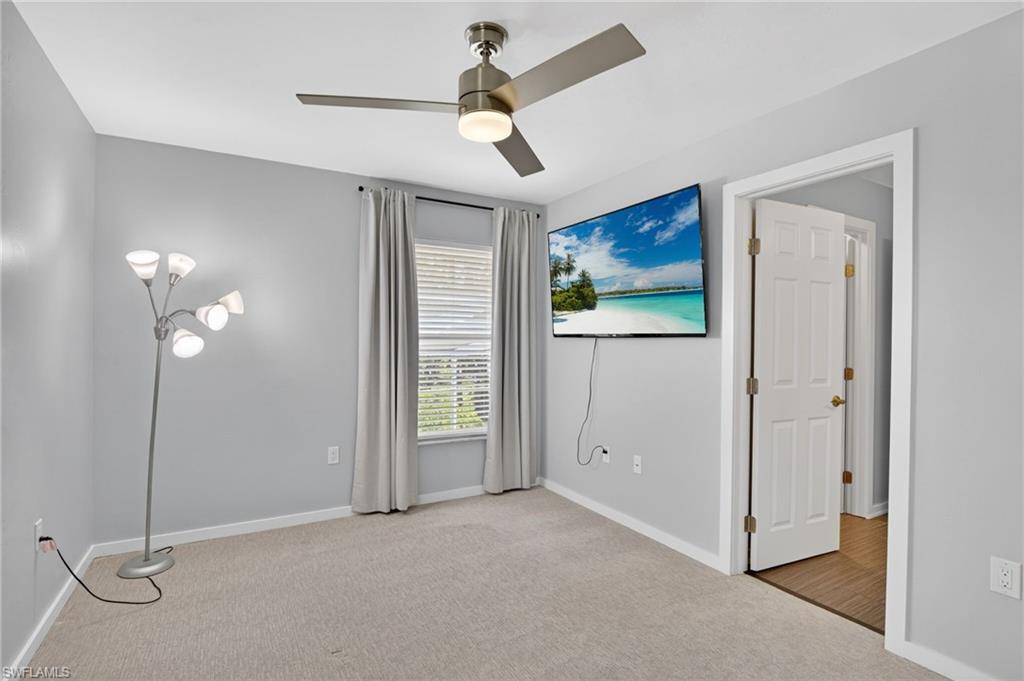Carpeted interior room featuring light gray wall paint, white trim, and a ceiling fan with brushed nickel accents