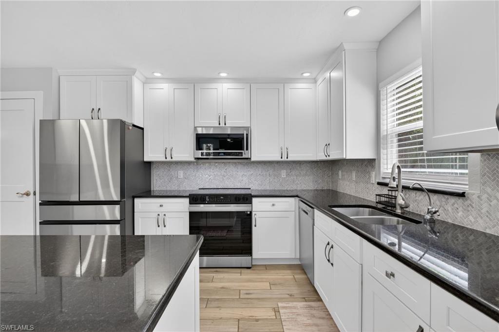 Modern kitchen featuring white shaker cabinetry, dark countertops, a herringbone tile backsplash, stainless steel appliances, and wood-finish flooring