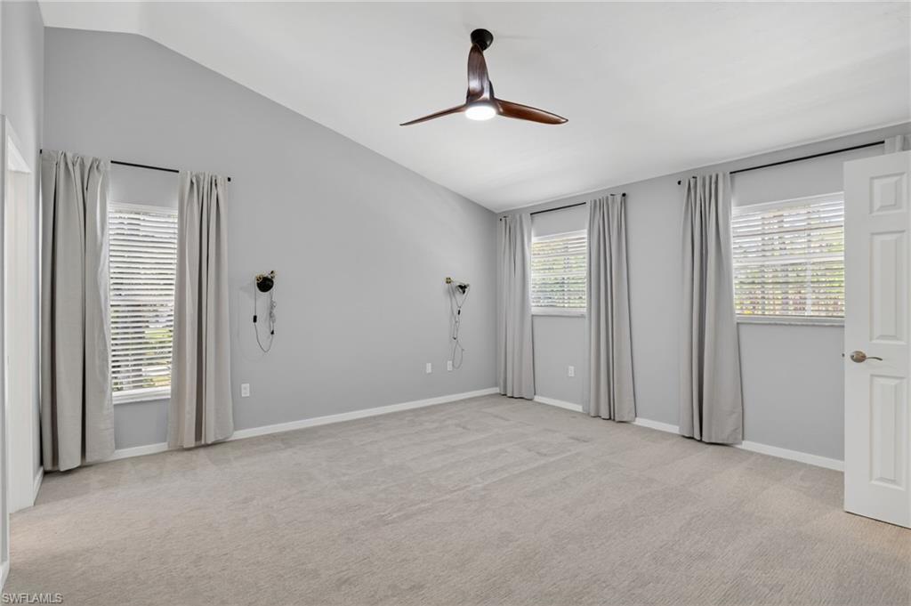 Spacious room featuring vaulted ceilings, light gray wall paint, and gray carpeted flooring