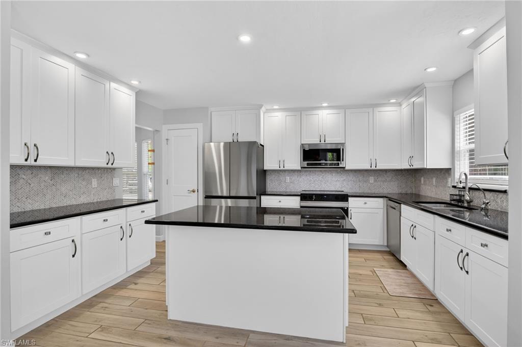 Kitchen featuring white cabinetry, dark countertops, a central island, stainless steel appliances, and wood-finish flooring
