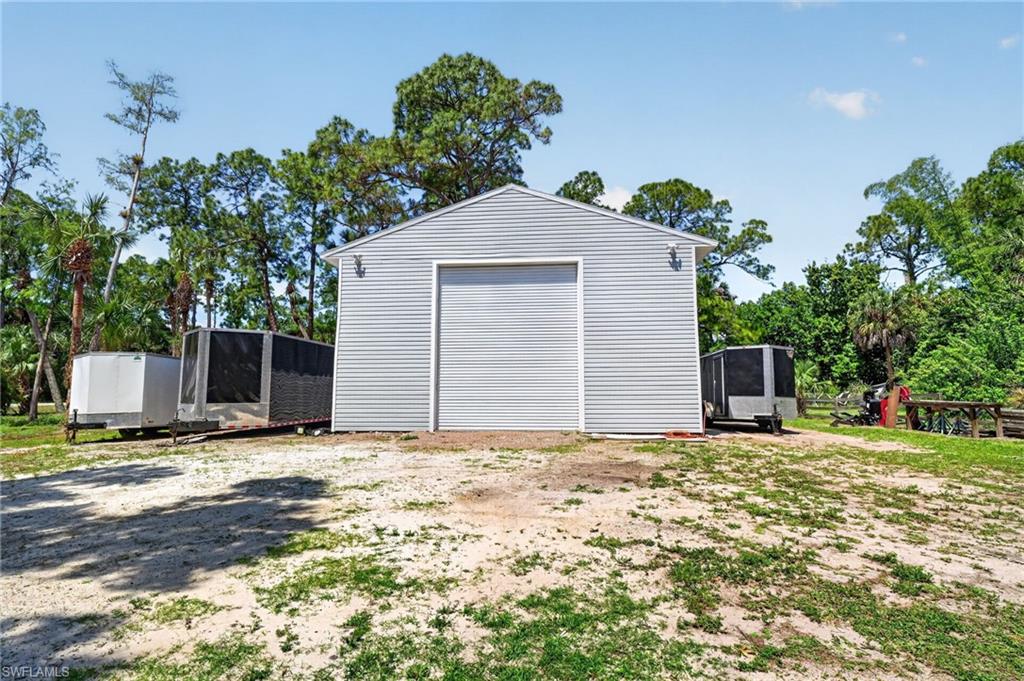 Light gray metal-sided outbuilding featuring a prominent roll-up garage door and exterior wall sconces