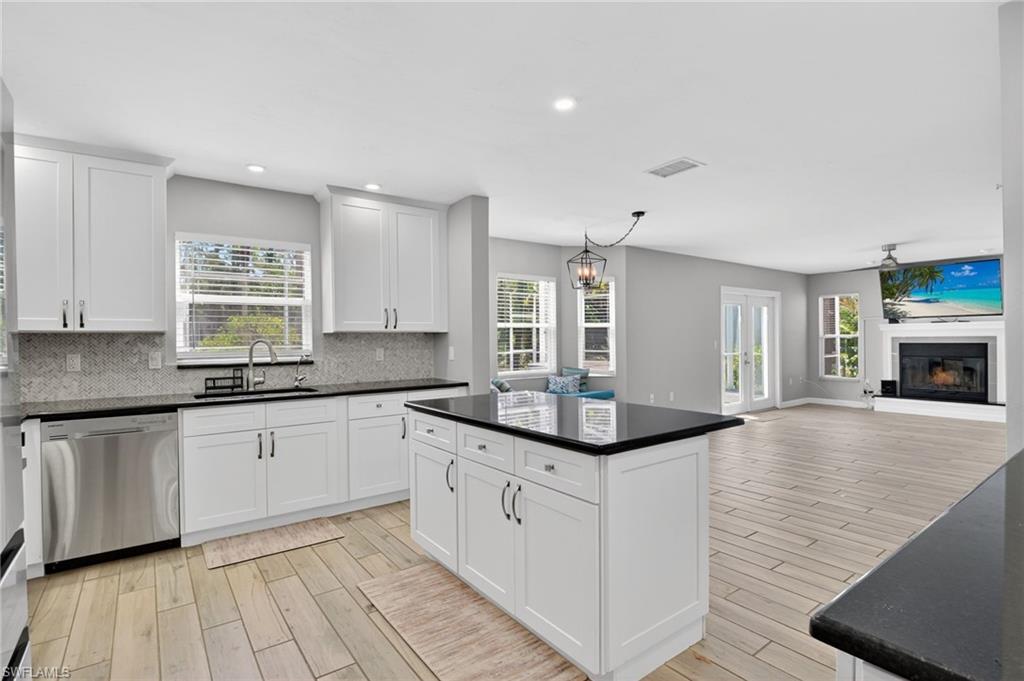 Open-concept kitchen featuring white cabinetry, dark countertops, a mosaic tile backsplash, and stainless steel appliances