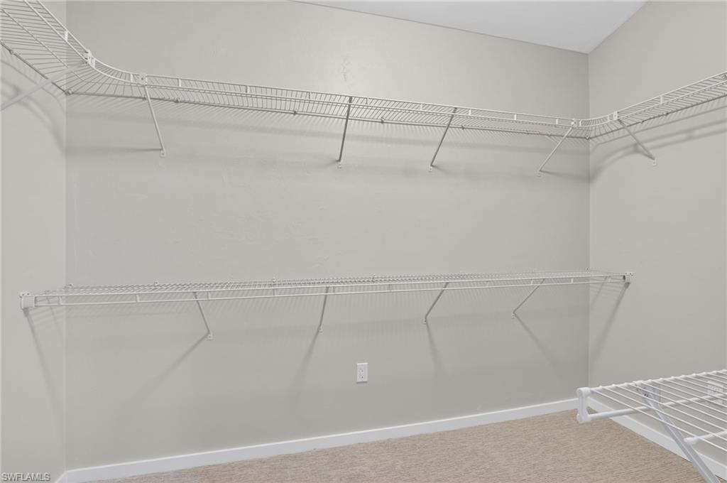 Spacious walk-in closet featuring light gray walls, white wire shelving, white baseboards, and neutral carpet flooring