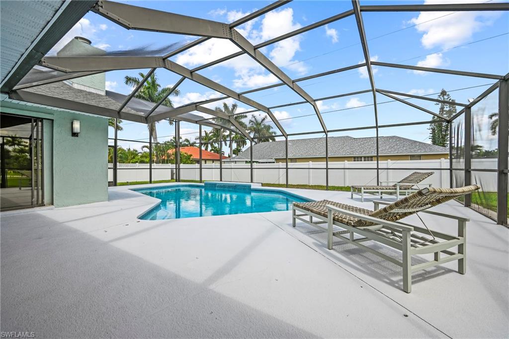 Screened outdoor living area featuring a freeform swimming pool, extensive white concrete decking, and a white privacy fence