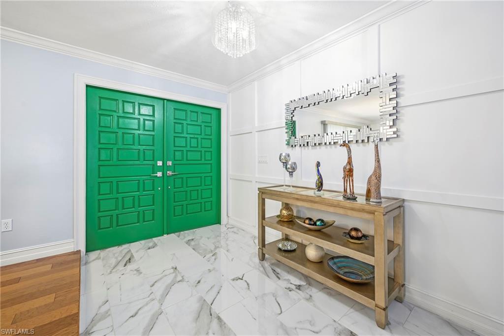 Entryway featuring double panel doors, marble-look flooring, decorative wall paneling, and crown molding