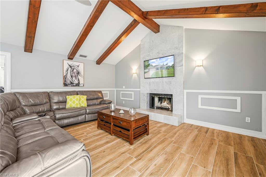 Vaulted ceiling with exposed wood beams, wood-finish flooring, and wainscoting