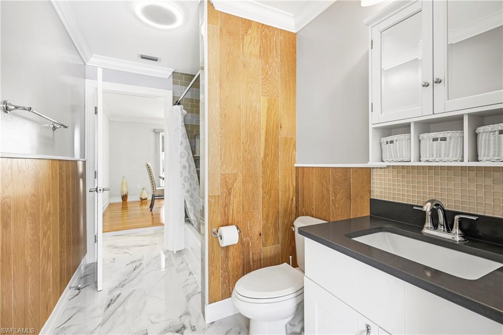 Bathroom featuring a white vanity with a dark countertop, square tile backsplash, and overhead storage cabinetry
