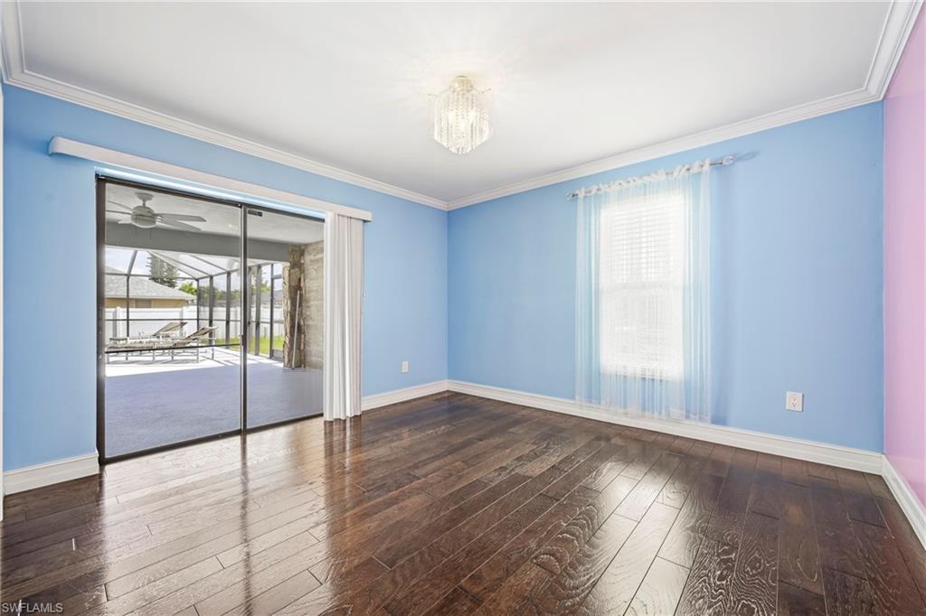 Spacious room featuring rich wood-finish flooring, crown molding, and an elegant chandelier