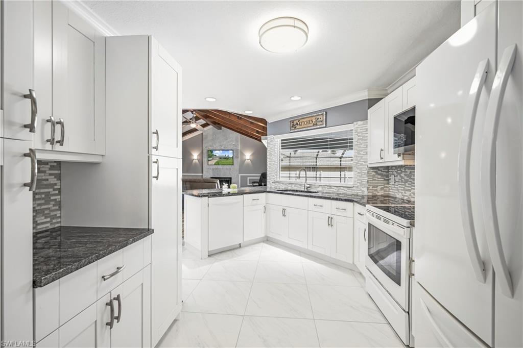 Modern kitchen featuring white cabinetry, dark granite countertops, a patterned tile backsplash, white appliances, and tiled flooring