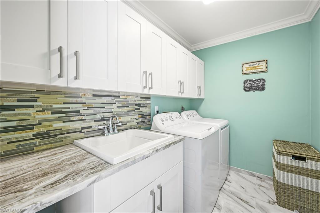 Laundry area featuring white shaker cabinetry, a utility sink with a chrome faucet, a patterned tile backsplash, and stone-look countertops