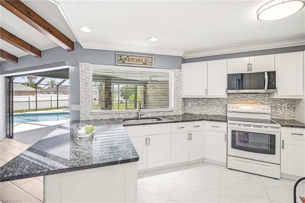 Bright kitchen featuring white cabinetry, dark stone countertops, and a white subway tile backsplash