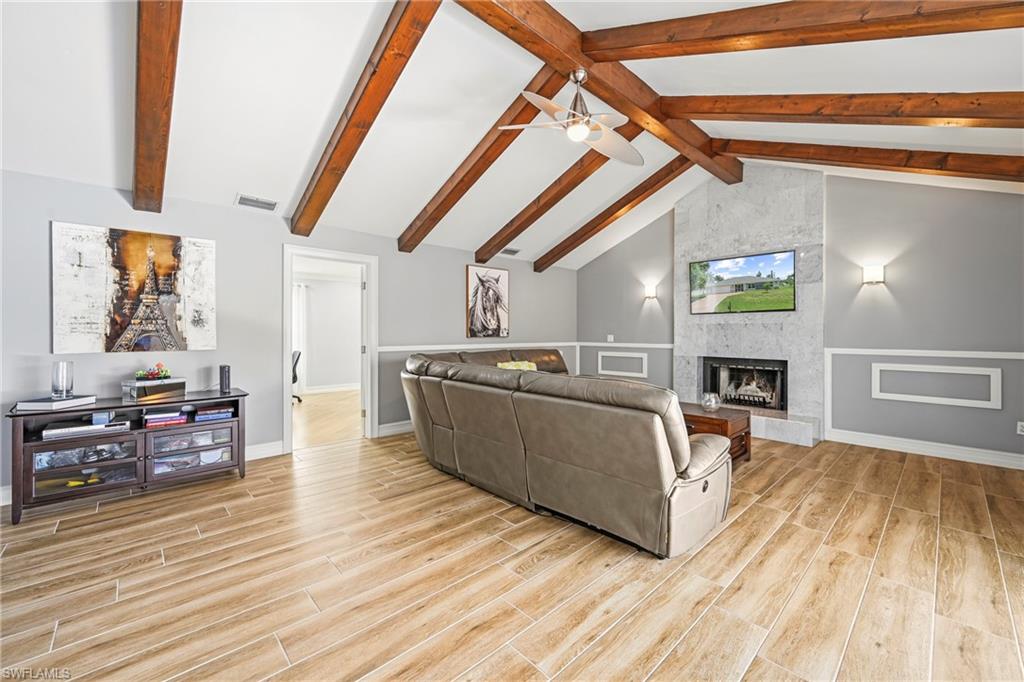 Vaulted ceiling with exposed wood beams, wood-finish flooring, accent fireplace with stone surround, wainscoting, and recessed lighting