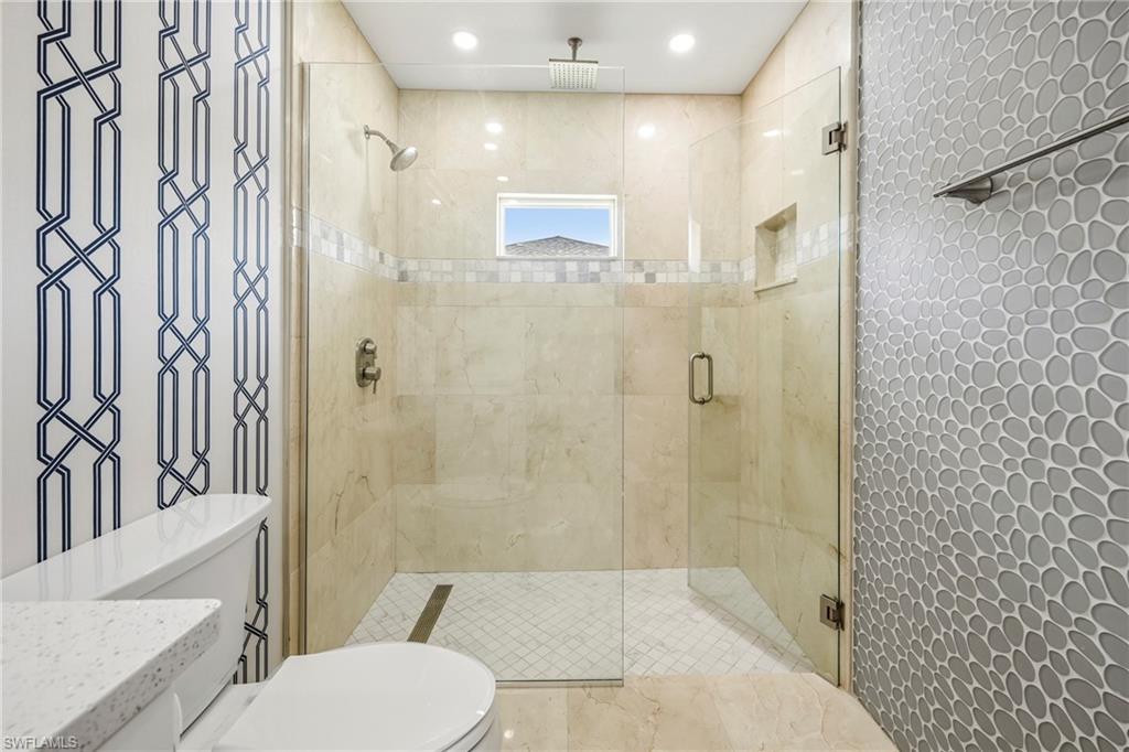 Frameless glass shower enclosure featuring a rain shower head, hand-held sprayer, built-in niche, and transom window